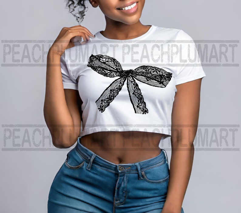 K&ouml;nnte beinhalten: Ein wei&szlig;es, bauchfreies T-Shirt mit einem schwarzen Spitzenbogen-Design. Das Shirt wird von einer Person mit dunkler Haut und kurzen, lockigen Haaren getragen. Die Person tr&auml;gt eine blaue Jeans.