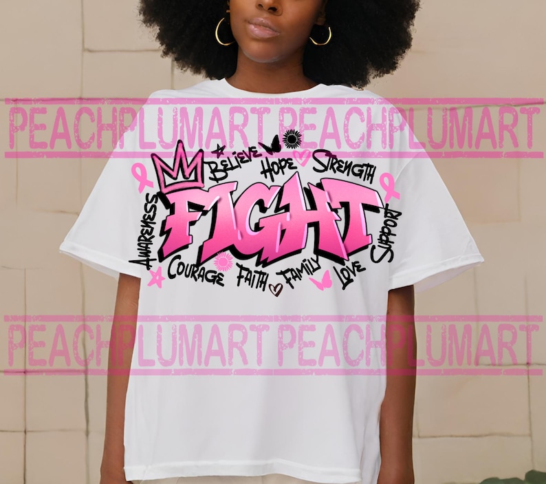 Op de afbeelding: Wit T-shirt met een roze grafisch ontwerp met de tekst "FIGHT" in grote letters. De grafiek bevat ook de woorden "Believe", "Hope", "Strength", "Awareness", "Courage", "Faith", "Family", "Love" en "Support".