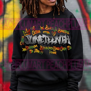 May include: Black sweatshirt with a graphic design featuring the word "Juneteenth" in silver with colorful accents. The design also includes the words "Strong", "Culture", "Black is Beautiful", "Freedom", "Breaking Every Chain", "June 19", and "Power".