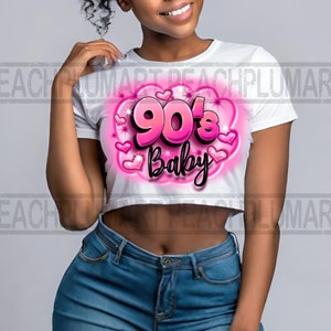 Könnte beinhalten: Weißes Crop-Top mit einem pinkfarbenen Grafikdesign, auf dem "90's Baby" steht, umgeben von pinkfarbenen Herzen und Glitzer.