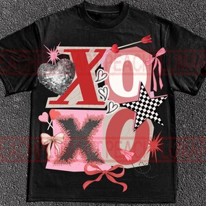 May include: Black t-shirt with a graphic design featuring the letters "XO" in red and pink, along with hearts, bows, and a checkered star. The design includes a disco ball heart and an arrow through a heart.
