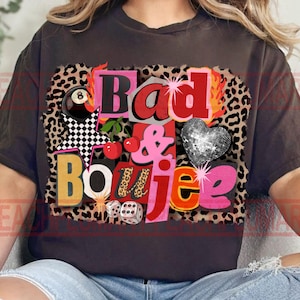 以下が含まれることがあります： 「Bad & Boujee」と書かれたカラフルなグラフィックが特徴の濃いグレーのTシャツ。デザインには、ヒョウ柄の背景、ディスコボールのハート、さくらんぼ、サイコロ、星が含まれています。 ゆったりとしたカジュアルなフィット感のTシャツです。