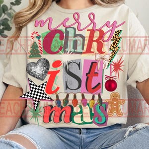 May include: Cream-colored t-shirt with a colorful Christmas-themed graphic. The design includes the words "merry Christmas" in pink, green, and red, along with festive images like a disco ball heart, a star, and a gingerbread man.