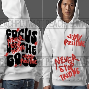 May include: White hooded sweatshirt with a black and red graphic print on the back that says "Focus on the good, never stop trying, stay positive". The front of the sweatshirt has a red graphic print that says "Stay positive, never stop trying".