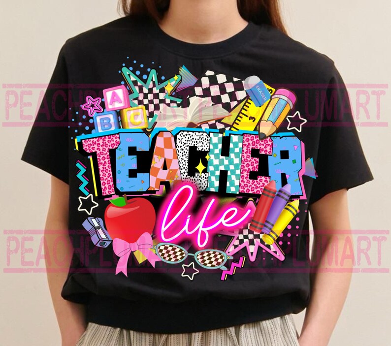 May include: Black t-shirt with a colorful "Teacher Life" graphic. The design includes an apple, pencils, crayons, and the words "Teacher Life" in a neon pink font. The word "Teacher" is in a mix of patterns and colors.