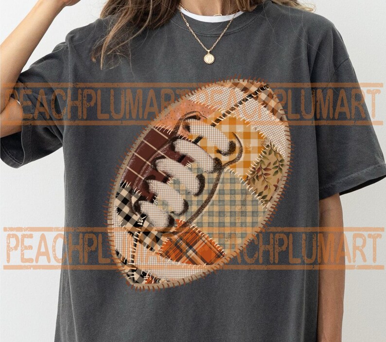 May include: Dark gray t-shirt featuring a football design. The football is made of patchwork fabric in shades of brown, orange, and cream. The design has a stitched outline and a white lace detail.