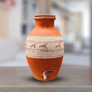 Pode incluir: Uma jarra de água de terracota com um design geométrico branco e castanho. A jarra tem uma torneira e uma tampa.