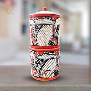 May include: A red and white ceramic water filter with a geometric pattern. The filter has a tap and a lid.