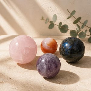 Peut inclure: Quatre sphères en pierre polie de tailles et de couleurs variées. Il y a un grand quartz rose pâle, une cornaline orange translucide plus petite, une labradorite gris foncé avec des reflets bleus et une améthyste violette de taille moyenne.