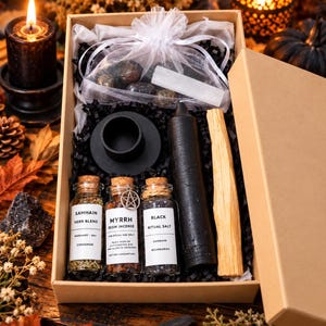 Può includere: Una scatola regalo in cartone contenente un sacchetto di organza bianco con cristalli e una bacchetta di selenite, un portacandele nero, una candela a colonna nera, un bastoncino di palo santo e tre barattoli di vetro etichettati Samhain Herb Blend, Myrrh Resin Incense e Black Ritual Salt.