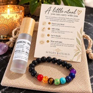 May include: A frosted glass essential oil roller bottle with a bamboo cap labeled Medicine Woman, alongside a black lava stone and multi-colored chakra bead bracelet. An instructional card titled A little ritual you can carry with you is included.