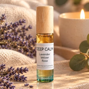 Könnte beinhalten: Eine Glas-Roll-on-Flasche mit hellem Holzdeckel und einem weißen Etikett mit der Aufschrift DEEP CALM, Lavender, Vetiver, Rose, Naturally Blended Essential Oils. Die Flasche enthält eine goldene Flüssigkeit und hat einen blaugrünen Boden.