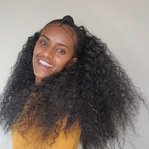 May include: A woman with long, curly black hair styled in a half-updo. She is wearing a yellow shirt.