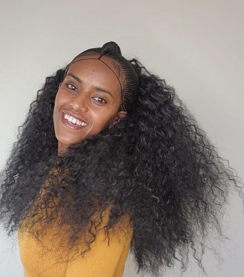 May include: A woman with long, curly black hair styled in a half-updo. She is wearing a yellow shirt.
