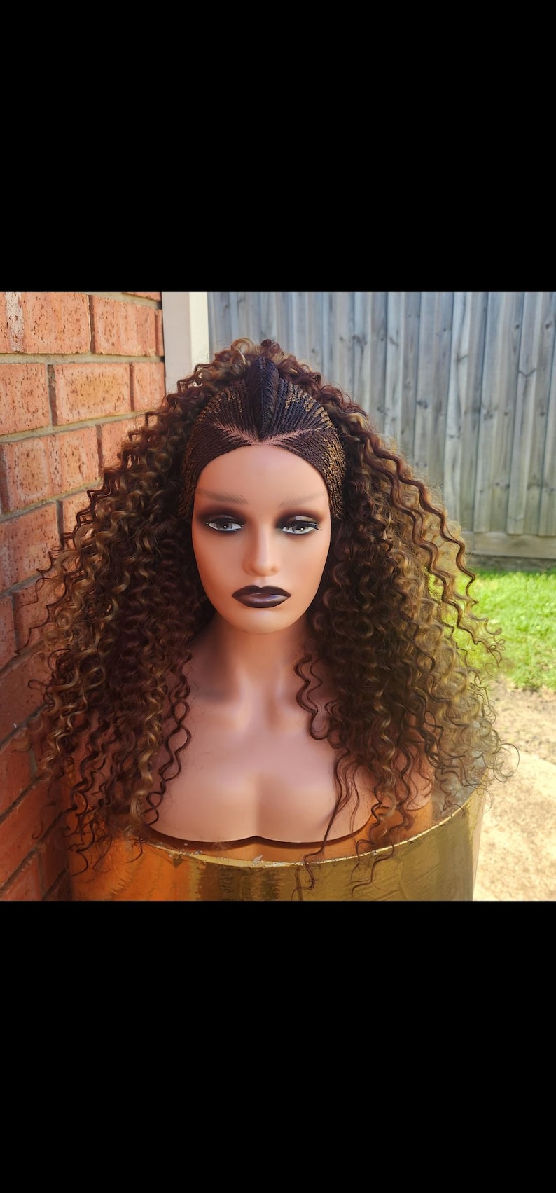 May include: A brown and blonde curly wig with a braided crown. The wig is on a mannequin head.