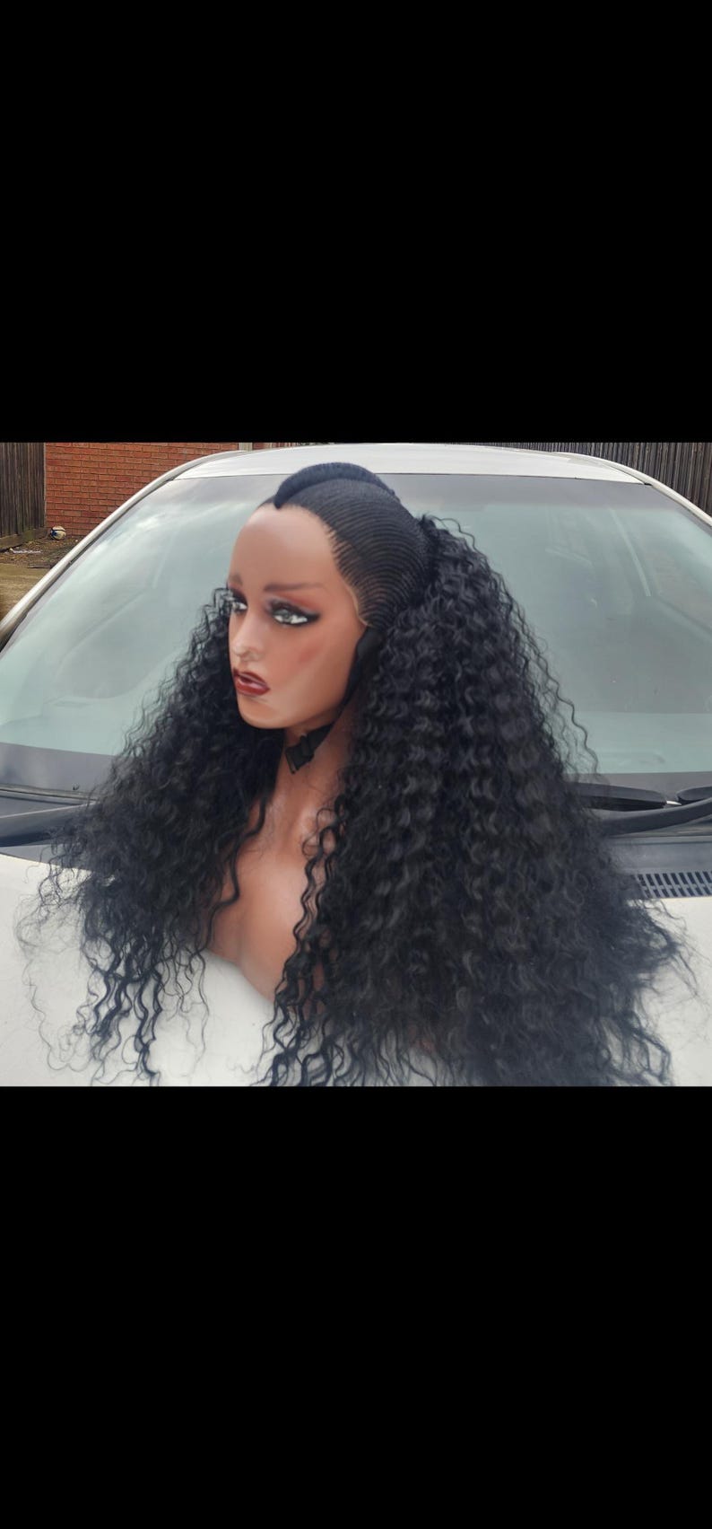 May include: A black curly human hair wig with a middle part and a high ponytail. The wig is styled in loose curls and is worn on a mannequin head.