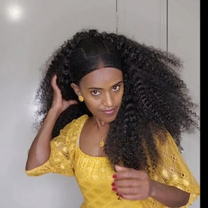 May include: A woman with long, curly black hair styled in a braided headband. She is wearing a yellow lace dress with a square neckline and red nail polish.