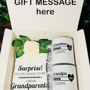 May include: A white gift box with a white shirt that says "Surprise! You're going to be babysitters... I mean Grandparents" and two white mugs that say "Grandma Loading... 2024" and "Grandpa Loading... 2024".