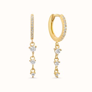 May include: A pair of gold-colored hoop earrings with a dangling design. Each earring features a row of small, clear stones along the hoop and three clear, heart-shaped stones suspended from the bottom.