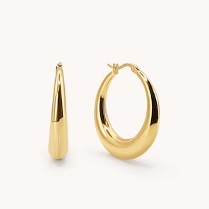May include: A pair of gold hoop earrings with a thick, rounded design. The earrings are made of metal and have a polished finish.