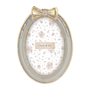 Peut inclure: Un cadre photo ovale avec une finition gris clair, des bords dorés et un nœud décoratif sur le dessus. L'insert central présente un fond clair avec un motif floral répétitif et le texte Clayre & Eef inscrit au milieu du cadre.