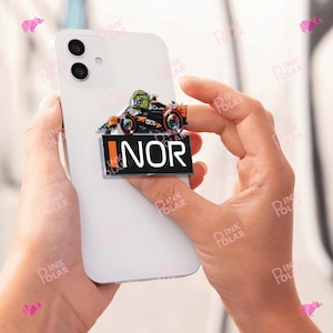 Könnte beinhalten: Ein Telefonzubehör mit einem Rennwagendesign in Orange, Schwarz und Grün. Das Zubehör hat den Text "NOR" auf schwarzem Hintergrund. Das Telefon ist weiß.