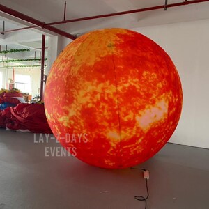 Op de afbeelding: Grote opblaasbare zon, voornamelijk oranje met gele details, voor een realistische uitstraling. De tekst "LAY-Z-DAYS EVENTS" staat linksonder op de opblaasbare zon. Geschikt voor evenementen.