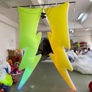 May include: Two large inflatable lightning bolt decorations, one neon green and one yellow, with internal LED lighting. The bolts are suspended from the ceiling, ideal for event decor. The text "LAY-Z-DAYS EVENTS" is visible on the bolts.