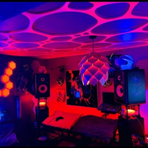 May include: A room illuminated by red and blue lighting, with a distinctive ceiling design featuring circular cutouts. A white, cone-shaped pendant light hangs from the ceiling. Speakers, artwork, and a bed are visible, suggesting a gaming or entertainment space.