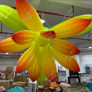 May include: Large inflatable flower decoration with vibrant colours. The petals transition from yellow to orange and red, with green leaves. The text "LAY-Z-DAYS EVENTS" is visible on the petals. This decorative piece is suitable for events and parties.