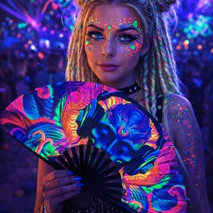 May include: A black hand fan featuring a swirling neon design in shades of blue, pink, orange, and green. The fan is held by a person with face paint and dreadlocks, in a crowd illuminated by neon lights.