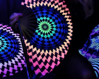 May include: Black hand fans with intricate geometric designs in neon colors. The fans feature a central floral pattern and a checkered pattern, with edges in pink, orange, and white. The fans are illuminated with a black light.
