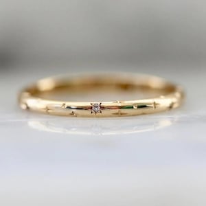 Puede incluir: Un anillo de oro con un pequeño diamante en el centro y grabados en forma de estrella. Esta delicada joya es ideal para el uso diario o para ocasiones especiales. El diseño es simple y elegante.
