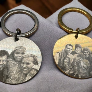 May include: Two silver and gold keychains with engraved photos of a family of four and a dog. The keychains are round and have a silver and gold ring.