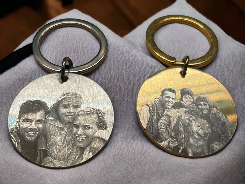 May include: Two silver and gold keychains with engraved photos of a family of four and a dog. The keychains are round and have a silver and gold ring.
