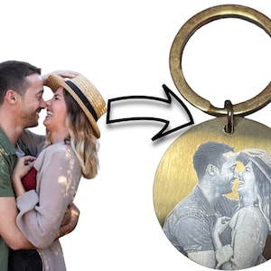 May include: A gold-toned keychain with a round metal charm featuring a black and white engraved image of a couple embracing.