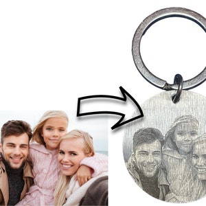 May include: A silver keychain with a round metal charm featuring a black and white engraved photo of a family of four. The keychain has a silver ring.