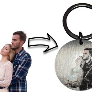 May include: A silver keychain with a round metal charm featuring a black and white photo of a couple embracing. The keychain has a black metal ring.