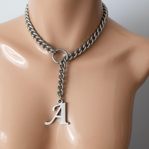 May include: A silver-toned chain necklace with a large, cursive letter "A" pendant. The necklace features a thick chain that encircles the neck, connected to a dangling chain and the pendant. The jewelry is displayed on a mannequin.