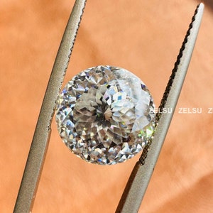 May include: A clear round diamond gemstone held by silver tweezers against a light brown background.