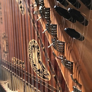 Puede incluir: Primer plano de un instrumento musical de madera con tallas intrincadas y una serie de clavijas de afinación. El instrumento tiene un cuerpo de madera y una serie de cuerdas que recorren la longitud del cuerpo.