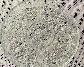 May include: A clear, round, divided serving dish with a starburst pattern. The dish is made of glass and has four sections, perfect for serving snacks or appetizers. The dish is approximately 12 inches in diameter.