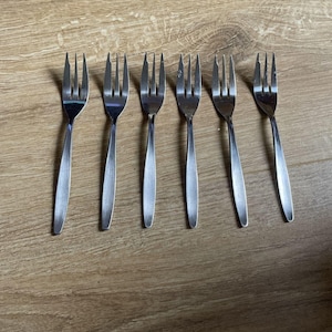 Op de afbeelding: Zes zilveren dessertvorken in een rij op een houten oppervlak.