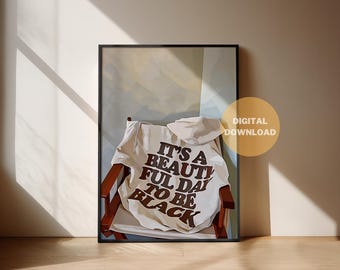 Puede incluir: Impresión artística enmarcada con una sudadera con capucha blanca sobre una silla de madera. La sudadera tiene el texto "IT'S A BEAUTIFUL DAY TO BE BLACK" en marrón. Descarga digital.