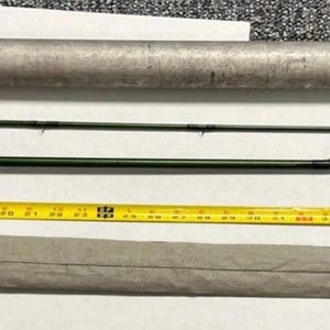 Puede incluir: Un conjunto de equipo de pesca, que incluye una caña de pescar con mosca con mango de madera, una cinta métrica y estuches protectores. La caña mide aproximadamente 244 cm de largo. Los artículos están dispuestos sobre una superficie blanca.
