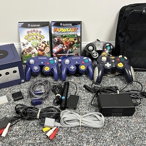 May include: A complete Nintendo GameCube set, including a purple console, controllers, games like "Monkey Ball 2" and "Mario Kart: Double Dash!!", and a black carrying case. Cables, power adapters, and memory cards are also included.
