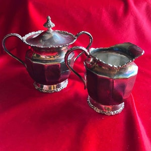 Könnte beinhalten: Ein silbernes Zucker- und Milchkännchen-Set mit verzierten Details. Die Teile haben eine geometrische, achteckige Form und sind aus poliertem Silber gefertigt.