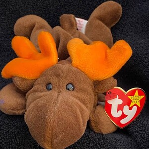 Può includere: Un alce marrone e arancione Ty Beanie Baby Moose con un'etichetta rossa a forma di cuore che dice "Beanie Original Baby" con una stella.