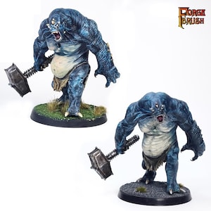 Puede incluir: Dos figuras en miniatura pintadas de azul y blanco de una criatura que sostiene un gran martillo de metal. Las figuras están de pie sobre bases circulares.