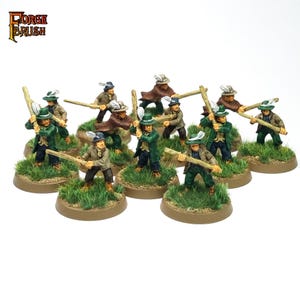 Puede incluir: Figuras en miniatura de figuras con abrigos verdes y marrones, sombreros con plumas y bastones de madera. Las figuras están sobre bases circulares con hierba. El logotipo de Forge Brush está en la esquina superior izquierda.